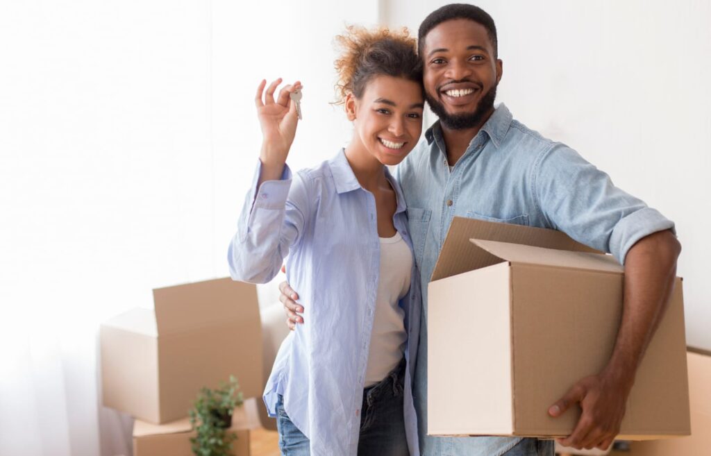 Young couple holding moving boxes in hands waving the new keys to their newly purchases home