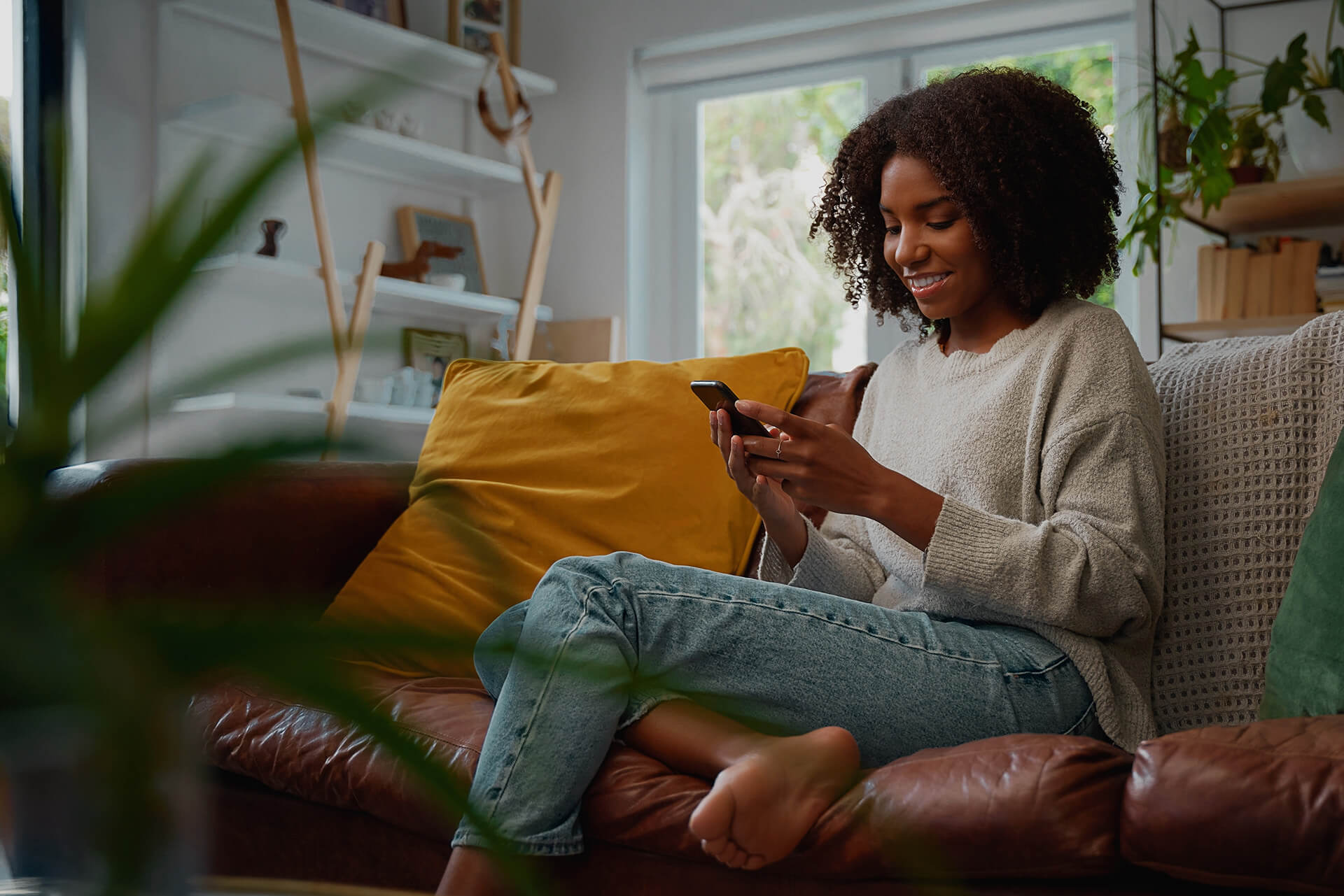 A young woman using QO Direct her phone while sitting on a couch.