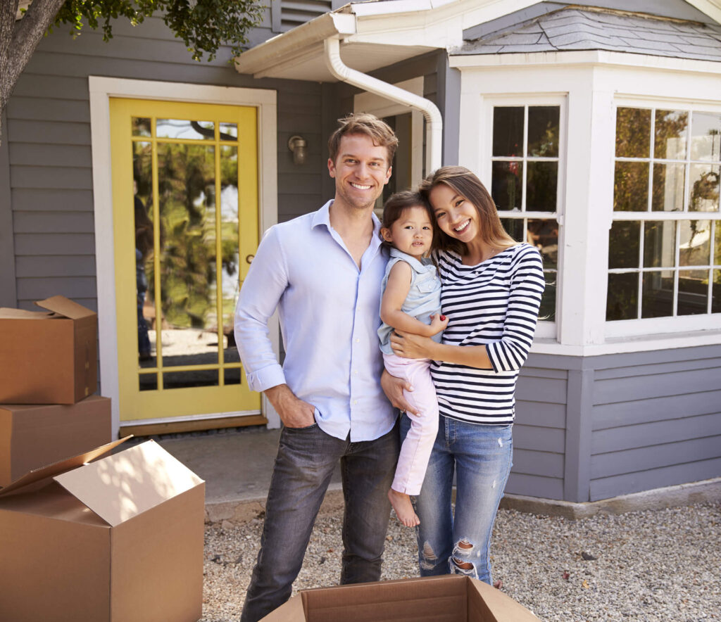 Young family standing in front of newly bought house financed with a conventional loan from Quaint Oak Mortgage