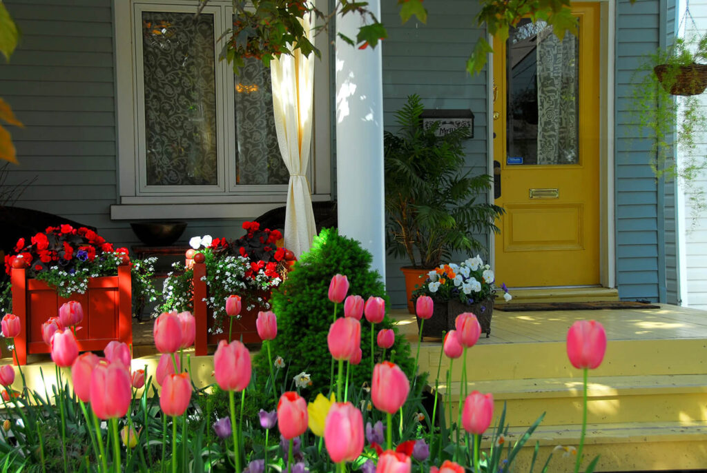 Gray house with yellow door with tulips on front walkway