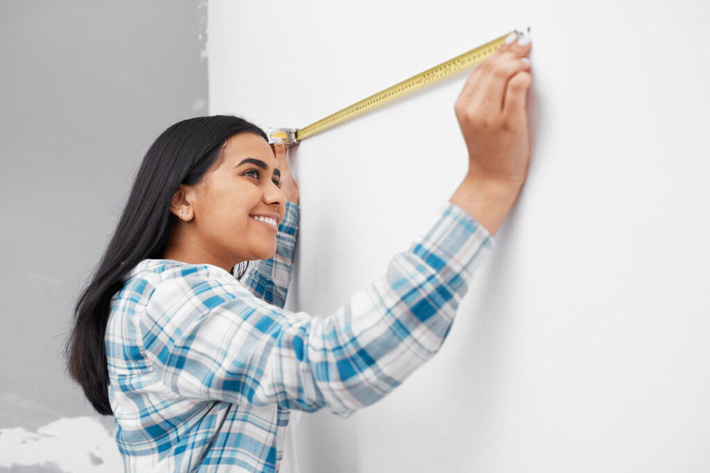 Woman using a tape measure on wall 