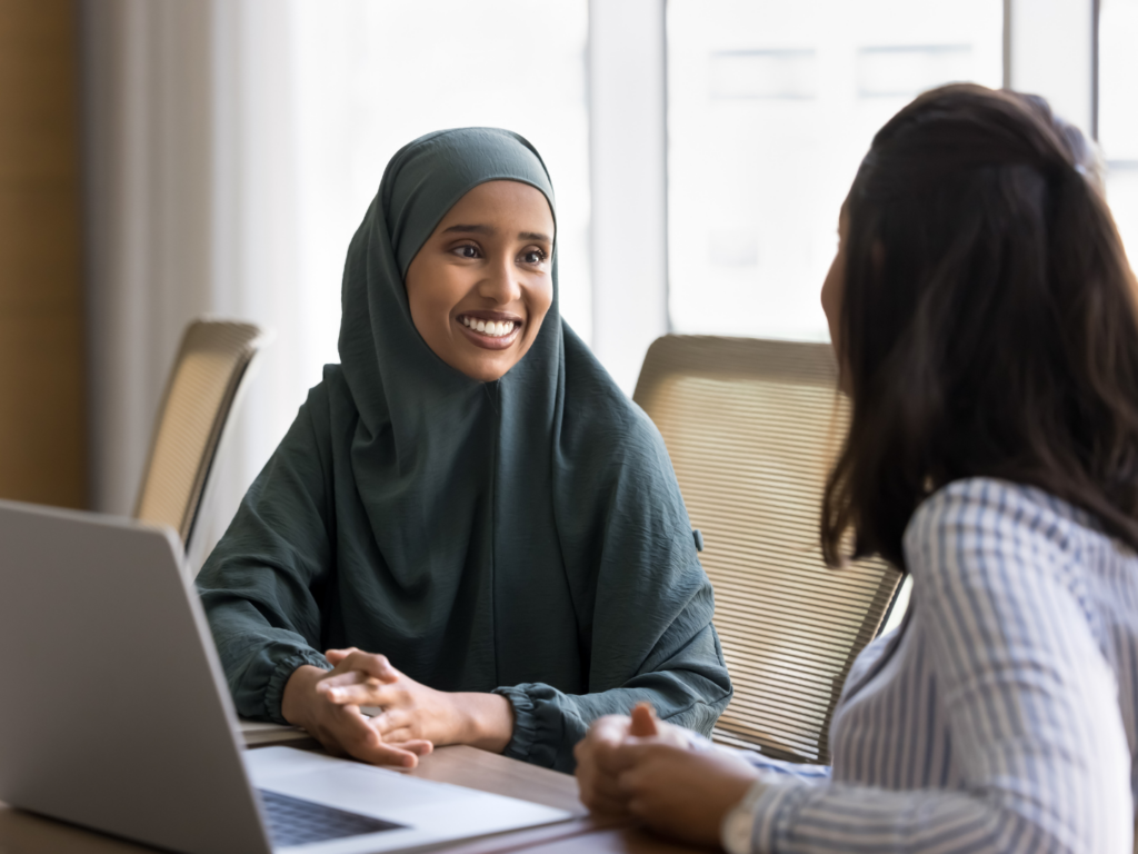 a woman wearing a traditional head covering sits at a table to meet with her lender to go over the common questions loan officers ask