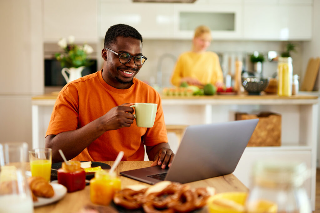 Man sitting at kitchen table looking at laptop.
