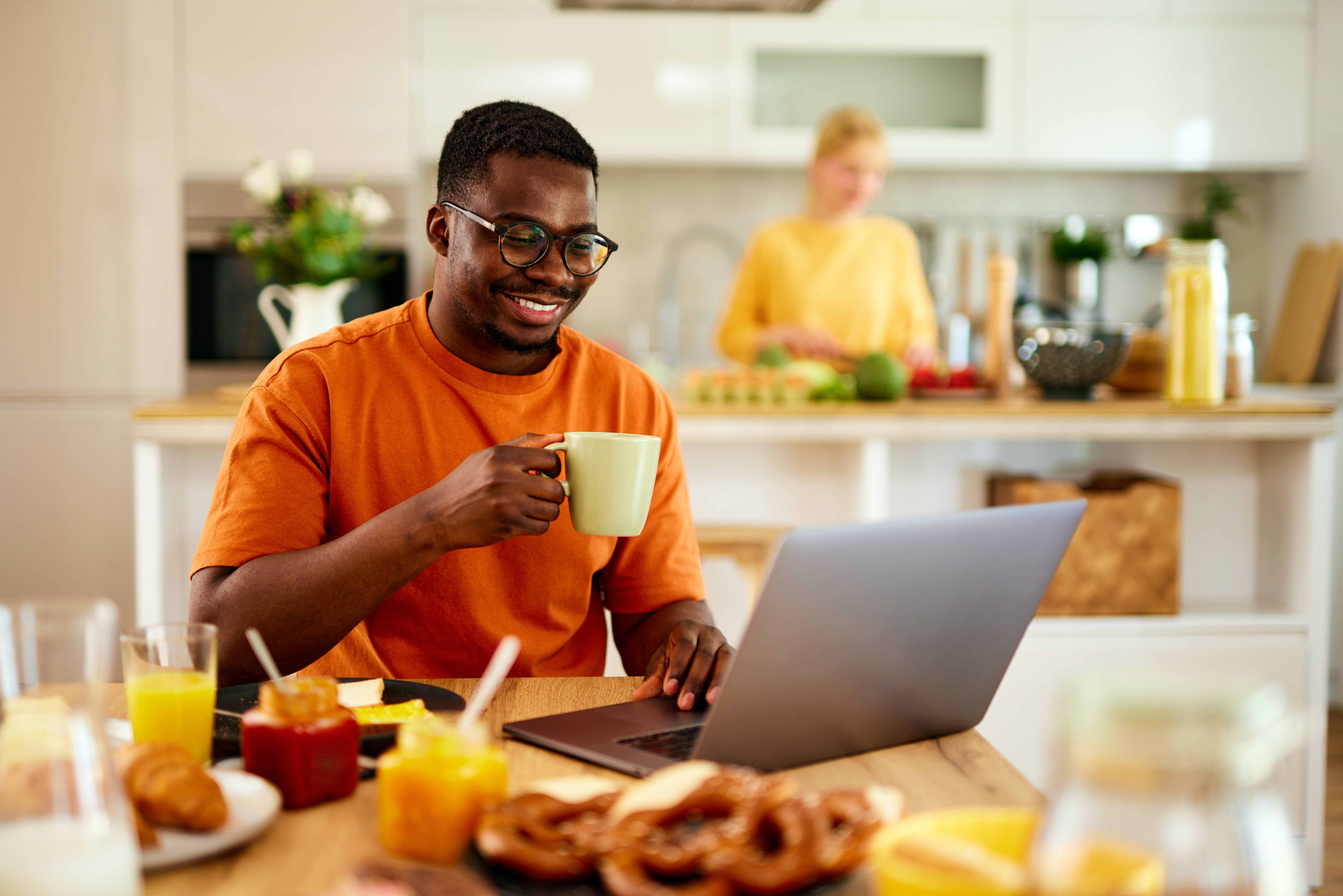 Man sitting at kitchen table looking at laptop.